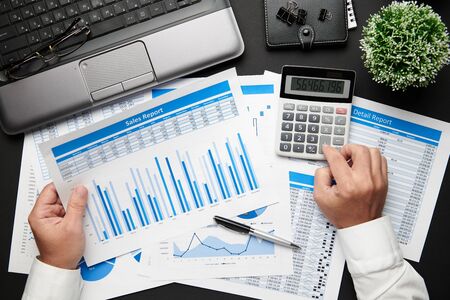 Top view of businessman's hands working with financial reports. Modern black office desk with laptop, notebook, pencil and a lot of things. Flat lay table layout.の写真素材