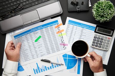 Top view of businessman's hands working with financial reports. Modern black office desk with...