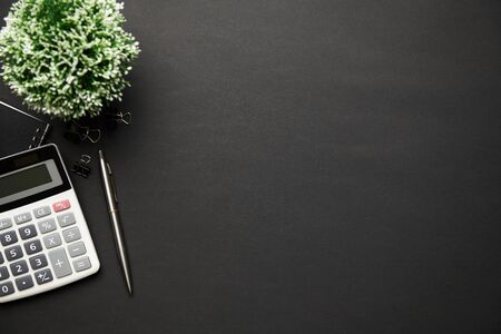 Top view of modern black office desk with calc, notebook, pen and a lot of things. Flat lay table layout. Copy space for text.の写真素材