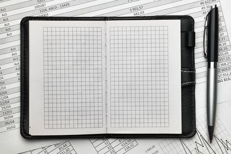 Top view of office employee's desk - empty Notepad with blank pages and financial reports, analysis...