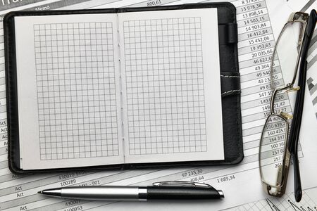 Top view of office employee's desk - empty Notepad with blank pages and financial reports, analysis...