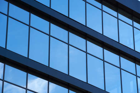 facade of a modern building on a bright Sunny day, blue sky and clouds reflecting in a glass,...
