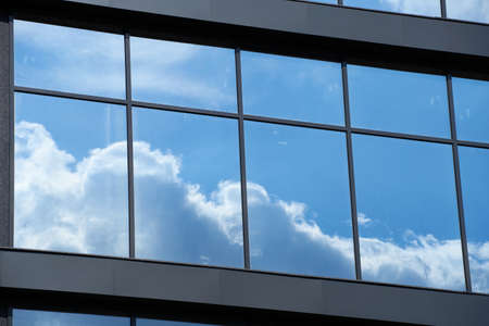 facade of a modern building on a bright Sunny day, blue sky and clouds reflecting in a glass,...