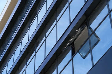 facade of a modern building on a bright Sunny day, blue sky and clouds reflecting in a glass,...