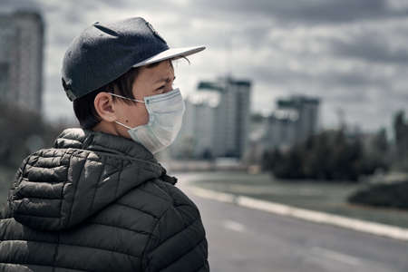 teenage boy poses in a city street, wearing a protective face mask - the concept of modern life and virus protectionの写真素材