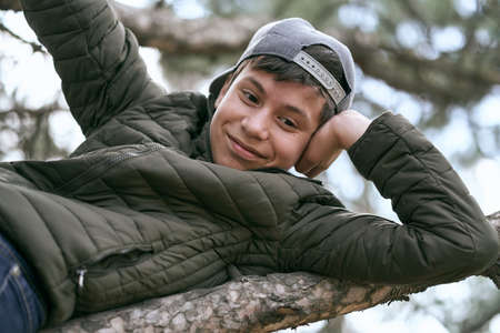 teenage boy poses on a tree, lying on a big branch and dreamingの写真素材