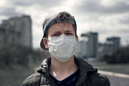 teenage boy poses in a city street, wearing a protective face mask - the concept of modern life and virus protectionの写真素材