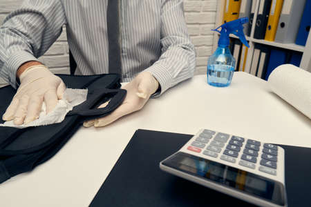 concept of cleaning or disinfecting the office desk - a businessman cleans the workplace, computer keyboard, document folders, uses a spray gun sanitizer, gloves and paper napkins.の写真素材