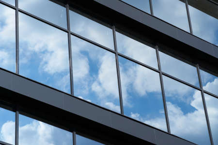facade of a modern building on a bright Sunny day, blue sky and clouds reflecting in a glass,...