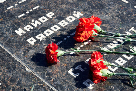flowers on the memorial to fallen soldiers, red carnations on black marble, Russian text of soldiers...