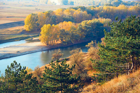 bright colorful autumn forest landscape, trees near river and blue sky, view from high hillの写真素材