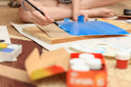 girl draws at home, artistic creation, makes creative artwork from paper, paints and brushesの写真素材