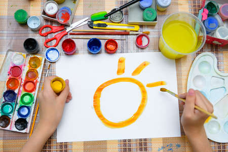 a girl drawing watercolor a big smiling sun on a blank white paper, artistic creation at home, makes...