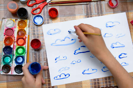 a girl drawing watercolor blue clouds on a blank white paper, artistic creation at home, makes creative artworkの写真素材