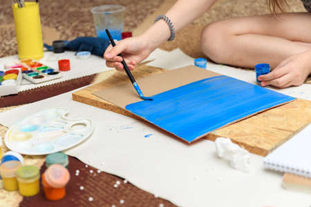 girl draws at home, artistic creation, makes creative artwork from paper, paints and brushesの写真素材