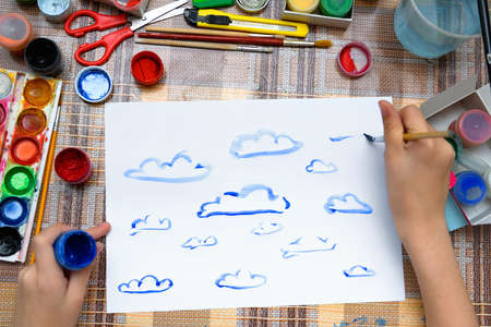 a girl drawing watercolor blue clouds on a blank white paper, artistic creation at home, makes creative artworkの写真素材