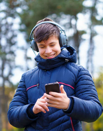 teenager listening to music by headphones, relaxing in autumn city park, using phone and sitting on a log, beautiful natureの写真素材