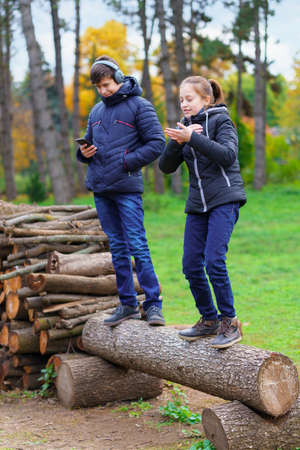 teens relaxing outdoor in autumn city park, happy people together, boy and girl, they standing on a log, playing, talking and smiling, beautiful natureの写真素材