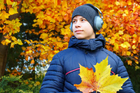 portrait of a teenager listening to music by headphones, relaxing in autumn city park, bright yellow...