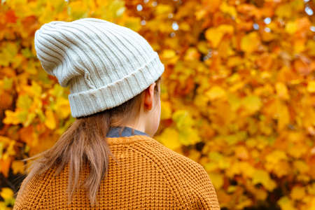 teen girl in autumn city park, looking on a background of yellow maple leaves and relaxing, she...