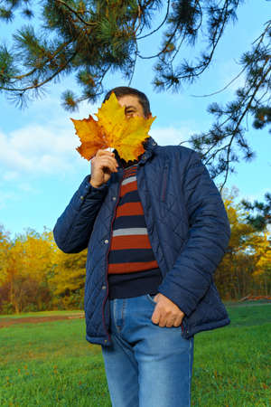 portrait of a man posing in autumn park, bright colorful leaves as backgroundの写真素材
