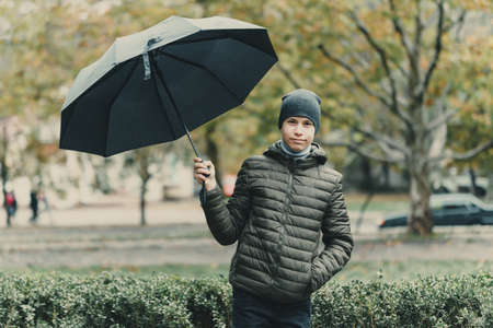 portrait of a teenager boy with umbrella, autumn season, city street
