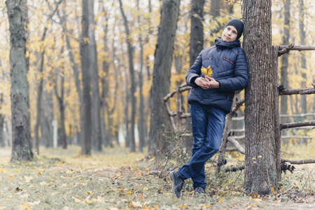 a boy posing in autumn park and having fun, showing a twig and grimacing, beautiful nature with yellow leavesの写真素材
