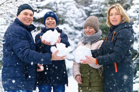 family portrait in the winter forest, parent and children, they make snowballs, beautiful nature with bright snowy fir treesの写真素材