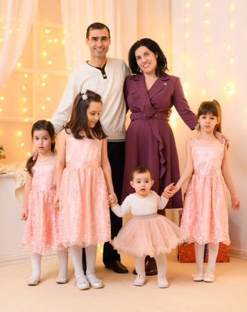 family portrait of a parents and children, sitting on a couch in home interior decorated with lights and giftsの写真素材