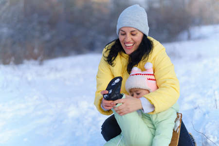 family portrait in the winter forest, mom straightens the baby's clothes and takes care, bright sunlight and shadows on the snow, beautiful nature.の写真素材