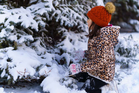 child girl sits and playing with snow in the winter forest, bright sunlight and shadows on the snow,...