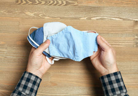 hands with selfmade breathing mask on a wooden background, checkered shirt in rustic styleの写真素材