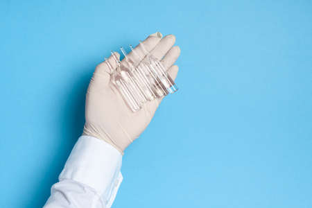 hands in medical gloves with ampoules of medicine or vaccine, blue background, imitation of a virus vaccine, prevention of infection with viruses and bacteriaの写真素材