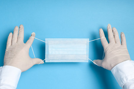 hands in medical gloves with a medical breathing mask on a blue background, health care prevention...
