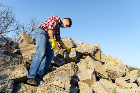 a man works with a pile of stones and broken pieces of concrete, carries construction debris
