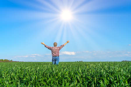 a man as a farmer poses in a field, dressed in a plaid shirt and jeans, he looks into the distance...