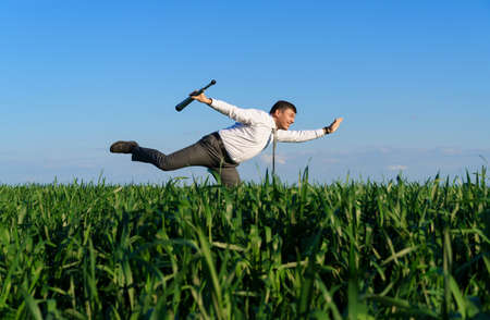 businessman poses with a spyglass, he looks into the distance and looks for something, green grass and blue sky as backgroundの写真素材
