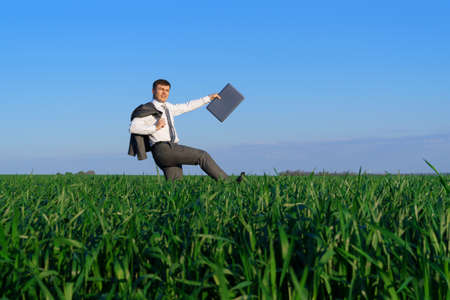 businessman poses with umbrella in a field, he's falling, a concept of crisis, green grass and blue sky as backgroundの写真素材
