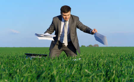 businessman sits in an office chair in a field and rests, freelance and business concept, green grass and blue sky as backgroundの写真素材