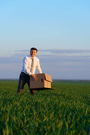 businessman walks through a green grass field and holds an office red folder with documents - business conceptの写真素材