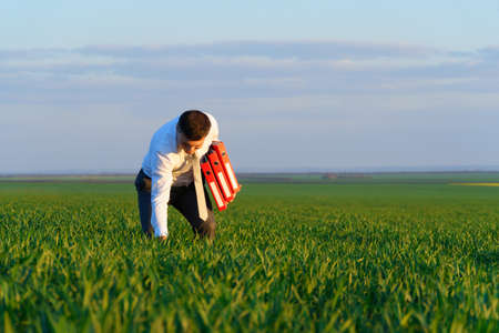 businessman walks through a green grass field and holds an office red folder with documents - business conceptの写真素材