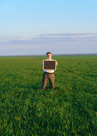 businessman walks through a green grass field and holds an office red folder with documents - business conceptの写真素材