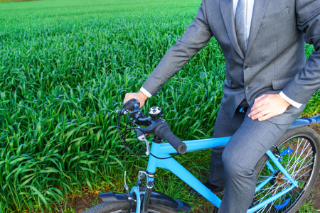 Businessman with a bicycle works with documents in a green grass field - business concept for freedom, vacation or freelance. Beautiful spring nature.の写真素材