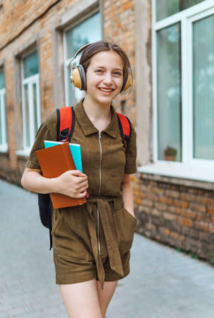 Teen schoolgirl on the way to the school. She is listening to music on headphones and holding a...