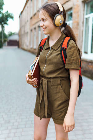 Teen schoolgirl on the way to the school. She is listening to music on headphones and holding a book. Education and back to school conceptの写真素材