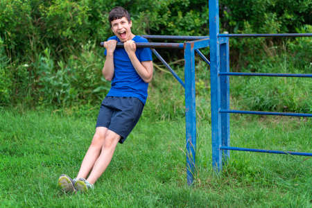 teenage boy exercising outdoors, sports ground in the yard, he squats and does a warm-up, healthy lifestyleの写真素材