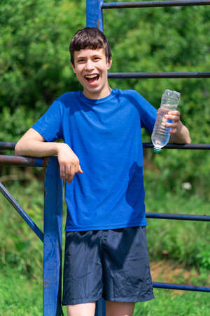 teenage boy exercising outdoors, sports ground in the yard, he squats and does a warm-up, healthy...