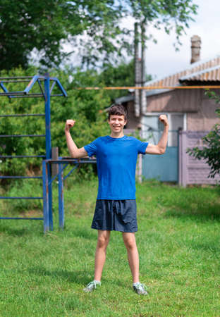 teenage boy exercising outdoors, sports ground in the yard, he hangs on the horizontal bar, raises...