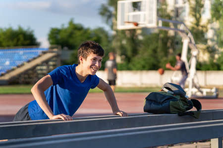 teenage boy exercising outdoors, sports ground in the yard, he hangs on the horizontal bar, raises his legs and shakes his abs, healthy lifestyleの写真素材
