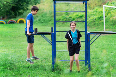 teenage boy exercising outdoors, sports ground in the yard, he posing at the horizontal bar, healthy...